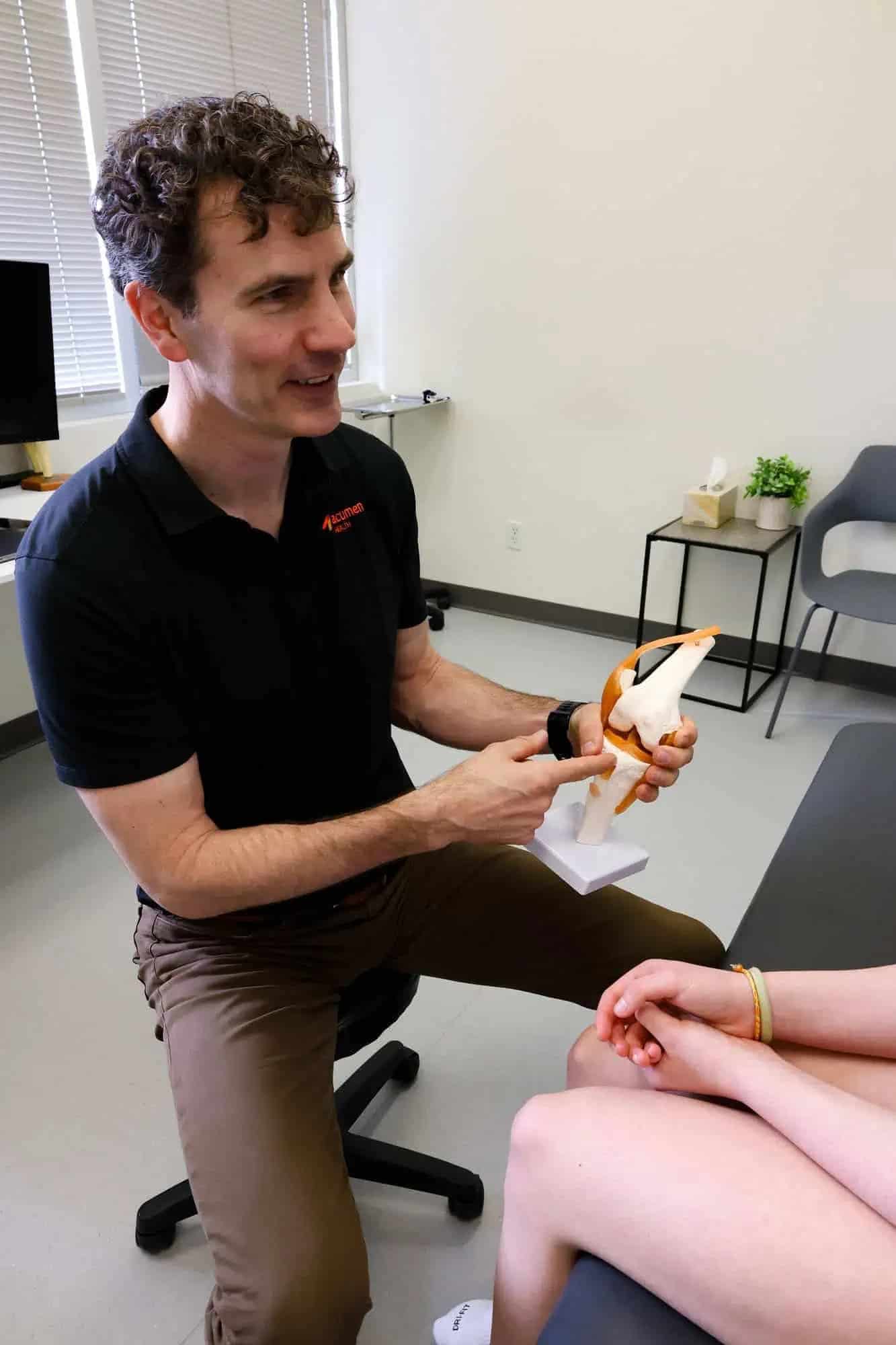 Clinician explaining knee anatomy model during private surgery consultation